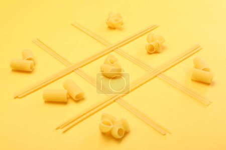 Tic tac toe game made with different types of pasta on yellow background
