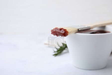 Marinade in bowl and basting brush on white table, closeup. Space for text