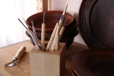 Conjunto de diferentes herramientas de elaboración y platos de arcilla sobre mesa de madera en taller, primer plano