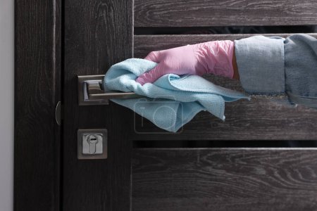 Woman wiping door handle with rag indoors, closeup