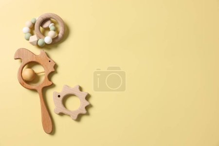 Baby accessories. Wooden rattles on yellow background, flat lay. Space for text