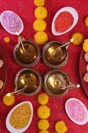 Diwali celebration. Flat lay composition with diya lamps and tasty Indian sweets on shiny red table