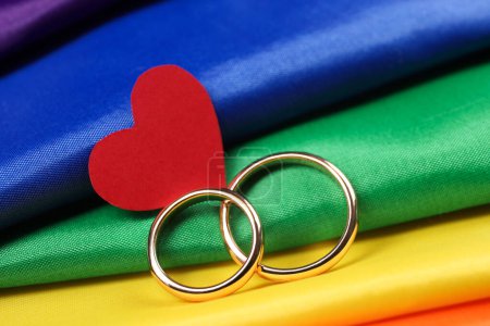 Wedding rings and heart on rainbow LGBT flag, closeup