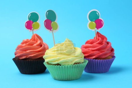 Delicious cupcakes with bright cream and toppers on light blue background