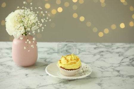 Delicious cupcake with yellow cream and flowers on white marble table against blurred lights