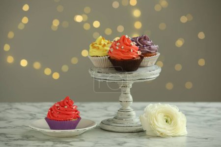 Different colorful cupcakes on white marble table against blurred lights