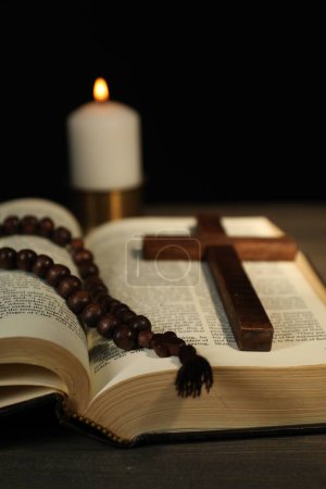 Kerze, Bibel, Rosenkranz und Kreuz auf Holztisch, Nahaufnahme