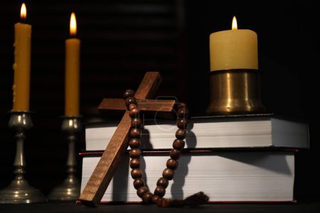 Velas de la Iglesia, Biblia, rosarios y cruz en la mesa en la oscuridad