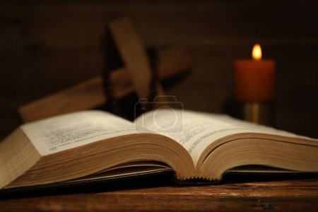 Bible, cross, rosary beads and church candle on wooden table, closeup