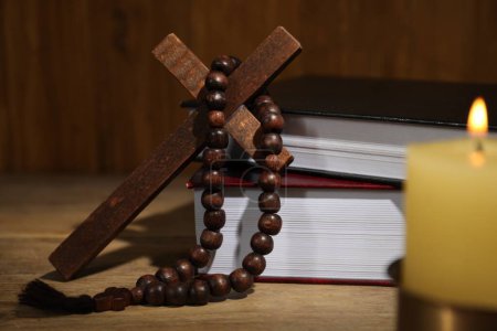 Bibel, Kreuz, Rosenkranzperlen und Kirchenkerze auf Holztisch