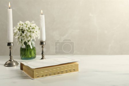 Photo for Burning church candles, Bible and flowers on white marble table. Space for text - Royalty Free Image