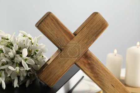 Wooden cross, Bible, flowers and church candles on table, closeup
