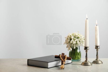 Bougies d'église, croix en bois, chapelet, Bible et fleurs sur table en marbre. Espace pour le texte