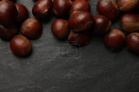 Roasted edible sweet chestnuts on grey textured table, flat lay. Space for text