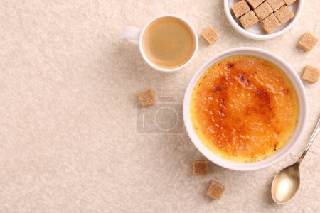 Deliciosa crema brulee en tazón, terrones de azúcar, café y cuchara en la mesa de textura ligera, la puesta plana. Espacio para texto