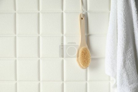 Accesorios de baño. Cepillo de bambú y toalla de rizo en la pared de azulejos blancos, espacio para el texto