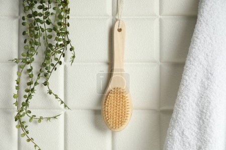 Photo for Bath accessories. Bamboo brush, terry towel and green plant on white tiled wall - Royalty Free Image