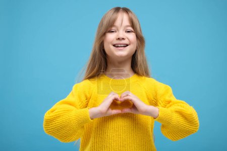 Glückliches Mädchen zeigt Herz-Geste mit Händen auf hellblauem Hintergrund