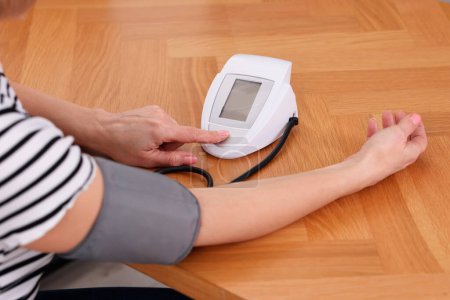 Foto de Mujer midiendo su presión arterial con tonómetro en mesa de madera en el interior, primer plano - Imagen libre de derechos