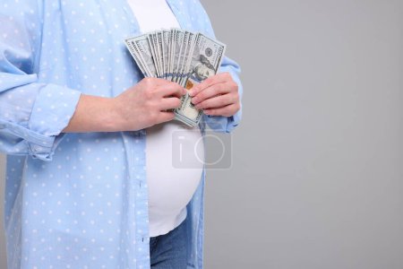 Téléchargez les photos : Mère porteuse. Femme enceinte avec des billets en dollars sur fond gris clair, gros plan. Espace pour le texte - en image libre de droit