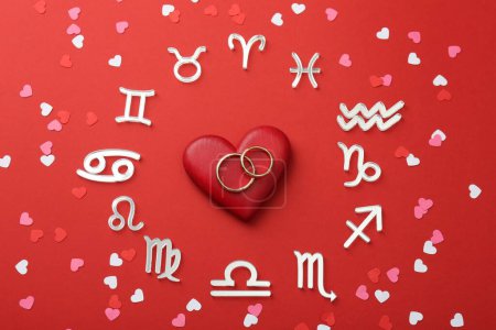 Foto de Signos del zodíaco, corazones y anillos de boda sobre fondo rojo, acostado plano - Imagen libre de derechos