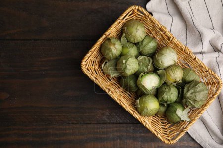 Fresh green tomatillos with husk in wicker basket on wooden table, top view. Space for text