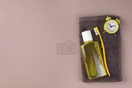 Foto de Enjuague bucal fresco en botella, cepillo de dientes, despertador y toalla sobre fondo beige, vista superior. Espacio para texto - Imagen libre de derechos