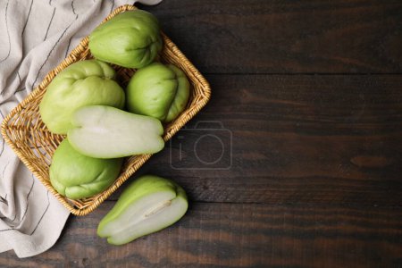 Photo for Cut and whole chayote in wicker basket on wooden table, flat lay. Space for text - Royalty Free Image