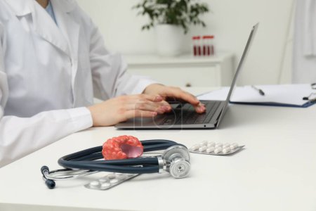 Endocrinologist working at table, focus on stethoscope and model of thyroid gland