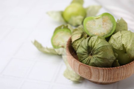 Frische grüne Tomatillos mit Schale in Schale auf weiß gefliestem Tisch, Nahaufnahme. Raum für Text