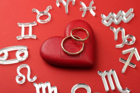 Zodiac signs, heart and wedding rings on red background