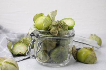 Tomatillos verts frais avec écorce dans un bocal en verre sur une table lumineuse, gros plan