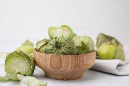 Tomates verdes frescos con cáscara en un tazón sobre una mesa de azulejos blancos, primer plano