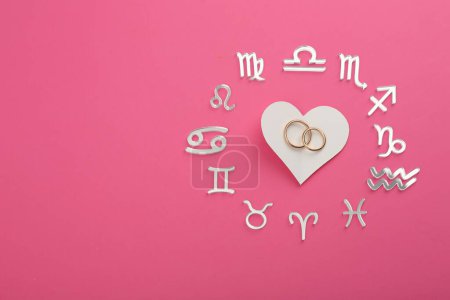 Foto de Signos del zodíaco, corazón y anillos de boda sobre fondo rosa, laico plano. Espacio para texto - Imagen libre de derechos