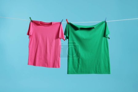 Zwei bunte T-Shirts trocknen auf Waschschnur vor hellblauem Hintergrund