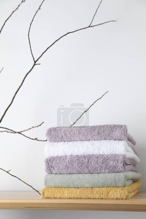 Gestapelte Frottee-Handtücher und Ast auf Holzregal in der Nähe der weißen Wand