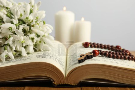 Bible, rosary beads, flowers and church candles on wooden table, closeup