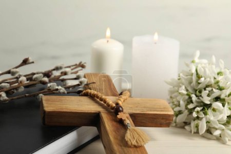 Photo for Burning church candles, wooden cross, rosary beads, Bible, willow branches and snowdrops on white table, closeup - Royalty Free Image