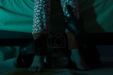 Téléchargez les photos : Monstre effrayant sous le lit saisir petite fille par les jambes dans l'obscurité, gros plan - en image libre de droit