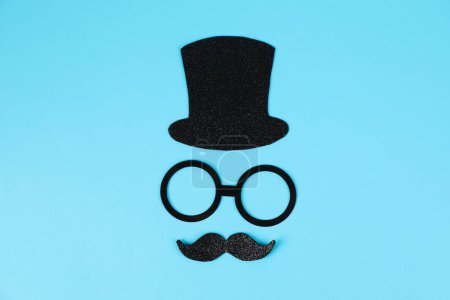 Téléchargez les photos : Visage d'homme en fausse moustache, chapeau et lunettes sur fond bleu clair, vue de dessus - en image libre de droit