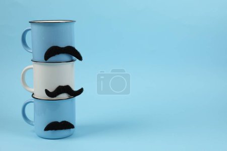 Téléchargez les photos : Tasses avec de fausses moustaches sur fond bleu clair. Espace pour le texte - en image libre de droit