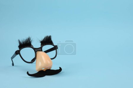 Téléchargez les photos : Masque drôle avec fausse moustache, nez et lunettes sur fond bleu clair. Espace pour le texte - en image libre de droit