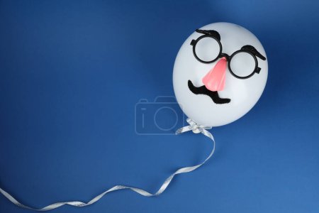 Téléchargez les photos : Visage d'homme en ballon, fausse moustache, nez et lunettes sur fond bleu, vue de dessus. Espace pour le texte - en image libre de droit