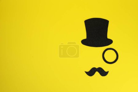 Téléchargez les photos : Visage d'homme en fausse moustache, chapeau et monocle sur fond jaune, vue de dessus. Espace pour le texte - en image libre de droit