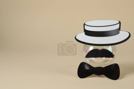 Téléchargez les photos : Visage d'homme en fausse moustache, boule, chapeau et noeud papillon sur fond beige. Espace pour le texte - en image libre de droit