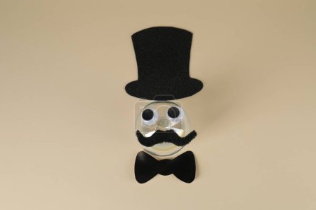 Téléchargez les photos : Visage d'homme en fausse moustache, boule, chapeau, noeud papillon et yeux sur fond beige, vue de dessus - en image libre de droit