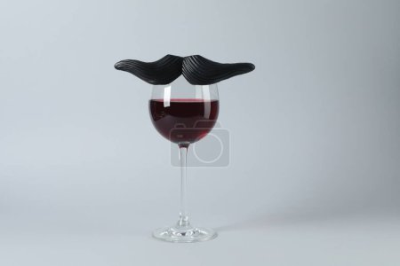 Téléchargez les photos : Verre de vin rouge avec drôle de fausse moustache sur fond gris - en image libre de droit