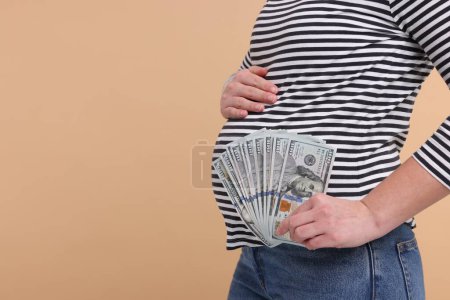 Téléchargez les photos : Mère porteuse. Femme enceinte avec des billets en dollars sur fond beige, gros plan. Espace pour le texte - en image libre de droit