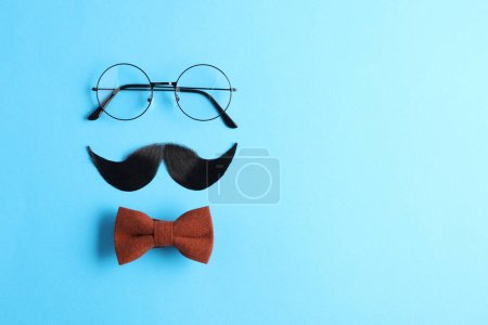 Téléchargez les photos : Moustache artificielle, noeud papillon et verres sur fond bleu clair, pose plate. Espace pour le texte - en image libre de droit