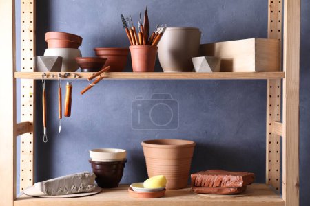 Ensemble de différents outils d'artisanat et plats en argile sur support en bois dans l'atelier